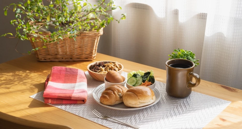 mesa de refeição posta, com pães, vegetais, ovo e prato e copo