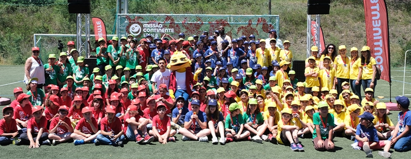 Muitas crianças com camisolas verdes, vermelhas, azuis e amarelas que participaram na escola Missão Continente